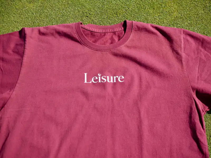 The burgundy logo tee up close — ribbed collar, the white Leisure logo across the chest